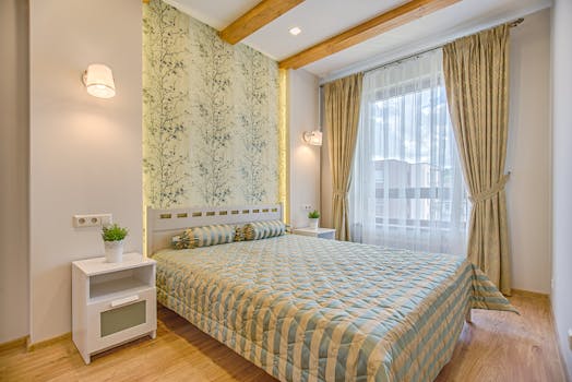 A luxurious and contemporary bedroom design with patterned wallpaper and natural lighting, located in Vilnius, Lithuania.